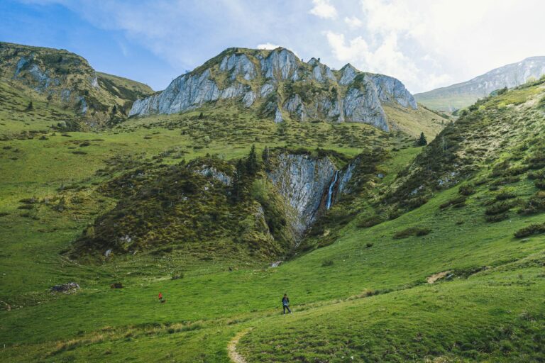 Hikers exploring a lush meadow with a waterfall in the French Pyrenees.