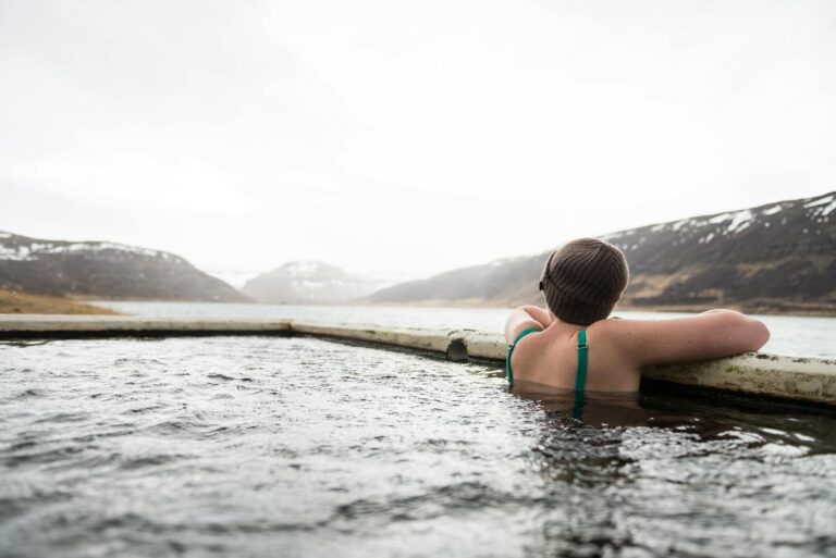 A person relaxes in a hot spring pool surrounded by snowy mountains and serene landscape.