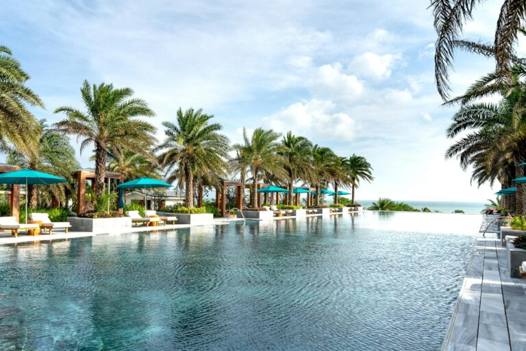 Relaxing scene of a luxury resort pool lined with palm trees and ocean view under a clear sky.