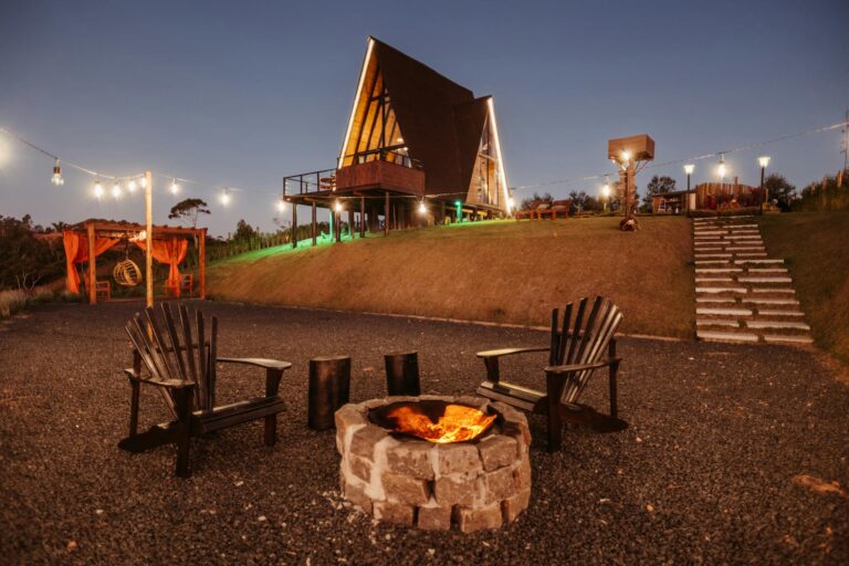 A serene evening at a firepit with an illuminated A-frame cabin in the background, perfect for leisure.