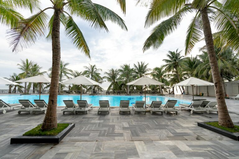 Relax by a tropical pool surrounded by palm trees and sun loungers in a sunny setting.