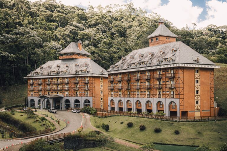 A picturesque Bavarian-style hotel surrounded by lush greenery and forest hillside.