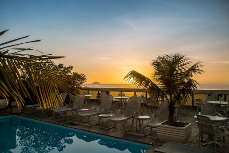 Relaxing tropical poolside scene with palm trees and lounge chairs at sunset.
