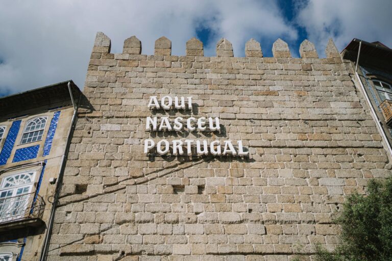 Medieval stone wall with 'Aqui Nasceu Portugal' sign in Guimarães under blue sky.